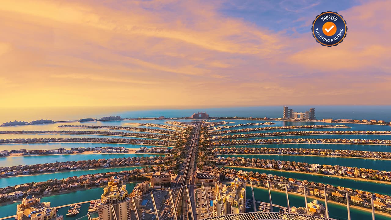 Aerial view of Dubai's Palm Jumeirah at sunset, highlighting the palm-shaped island, luxurious villas, and calm blue waters under a golden sky.