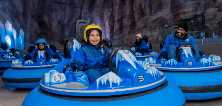 Children and adults enjoy bumper cars in an ice-themed indoor amusement park Snow Abu Dhabi. They wear blue jackets and helmets