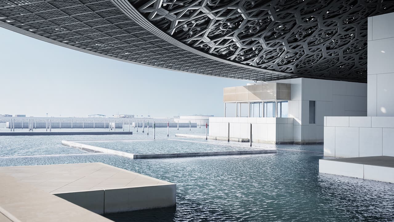 A large water section in Louvre Abu Dhabi in the background under a clear blue sky.