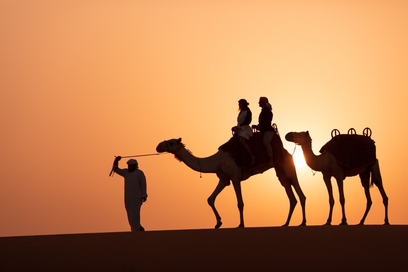 Guests enjoying a sunset camel ride during the Platinum Desert Safari experience in the Dubai desert.
