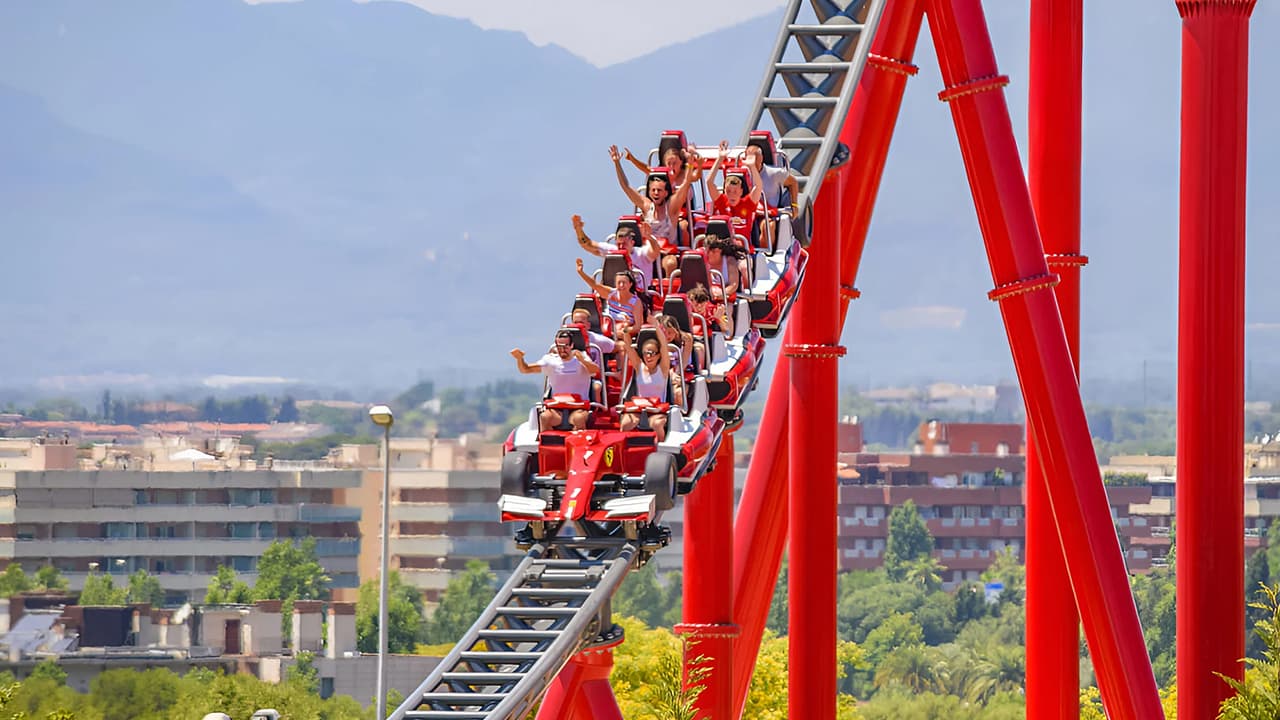 A group of excited people enjoying a thrilling ride on a roller coaster in Ferrari World Abu Dhabi, with their hands raised in the air.