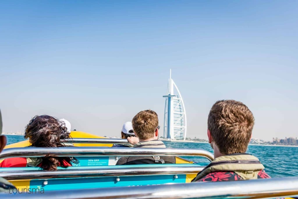 People on a speedboat gaze at the Burj Al Arab against a clear blue sky