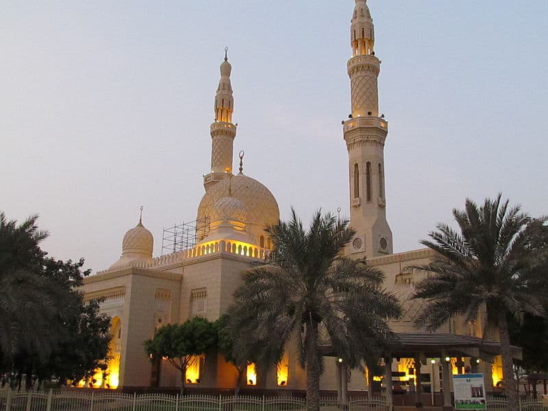 A grand mosque at dusk with illuminated domes and minarets. The warm glow contrasts with the darkening sky