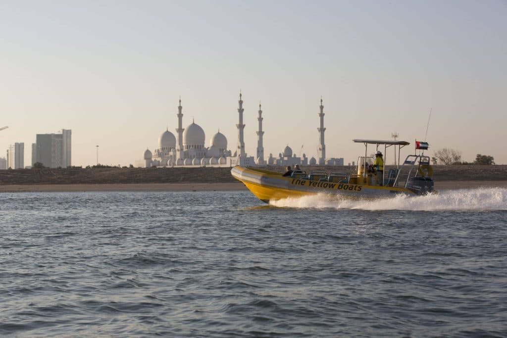 A yellow and white boat glides through the water near the Sheikh Zayed Mosque in Abu Dhabi.