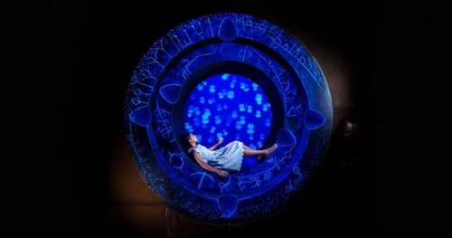 A woman sitting in a circle illuminated by blue lights at the Lost Chambers Aquarium.