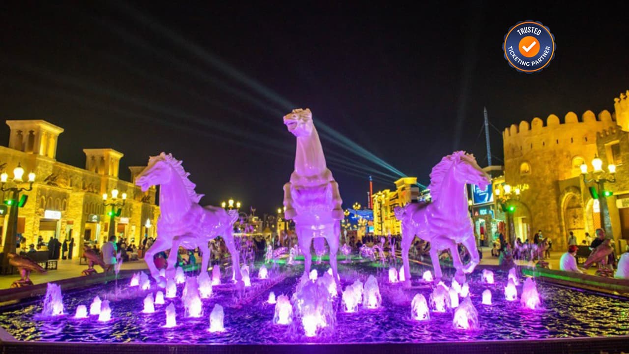 Illuminated horse statues rise from a vibrant purple fountain against a night sky.