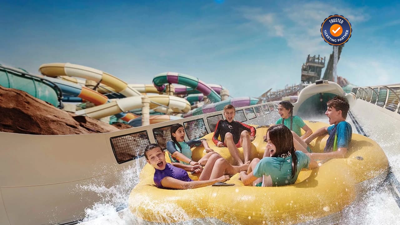 Group of six on a yellow raft ride in Yas Island water park, surrounded by colorful slides