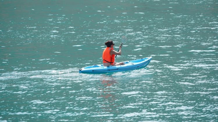 Person kayaking on calm, turquoise water, wearing an orange life jacket.