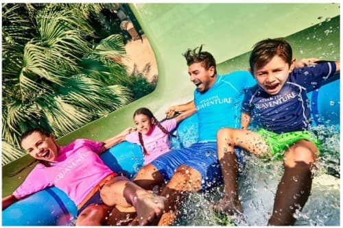 A family of four joyfully slides down a water slide at Dolphin Kayak Dubai, splashing into the water below.