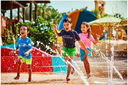 Three children splash and play joyfully in the water at Dubai Atlantis water park.