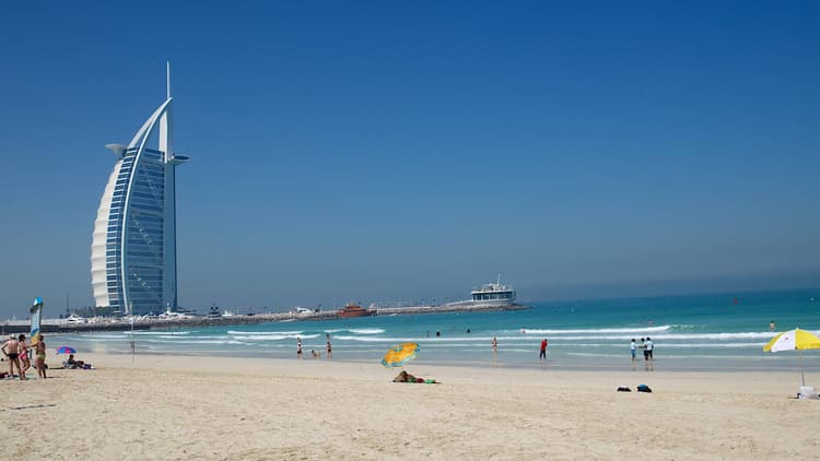 Beach scene with people lounging and swimming under a bright sun.