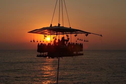 A restaurant suspended above the ocean, offering a stunning sunset view during Dinner In The Sky experience.
